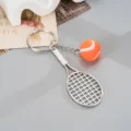 Metal tennis racket keychain with mini tennis ball pendant, stylish bag charm accessory. - Alloy Tennis Racket Pendant (K6727) / Orange
