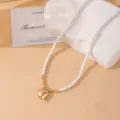 Primer plano detalle del collar de cuentas blancas con colgante de corazón dorado y soporte. - Estilo de Cuentas de Corazón / Blanco