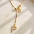 Vista detallada de un collar de oro delicado con dijes de letras brillantes en mármol. - Letra P