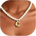 Detalle en primer plano de un elegante collar con colgante de letra C dorada y perlas. - Letra C