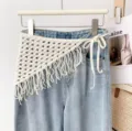 Detailed view of white crochet fringe triangular waist scarf accessory tied on blue jeans. - One Size / Apricot Fringe