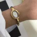 Nahaufnahme einer eleganten goldenen ovalen Armreif-Uhr mit weißem Zifferblatt. - Ovale Bangle Uhr mit Römischen Ziffern (878 Gold Hände) / Gold