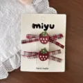 Deux clips fraise à pois blancs, feuilles vertes et nœuds rouges à carreaux, présentés sur une carte - Clip Fraise Brodé Carreaux Rouges (261011)