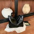 Black glossy PU tote bag with stud details and a fluffy pom-pom charm, styled on a wooden shelf - With Pendant / Black
