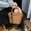 Brown woven-texture handbag with a round ring handle and bead charm, shown held indoors - With Pendant / Brown