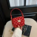 Petit sac à main rouge à pois, fermoir nœud et bandoulière chaîne, présenté devant un siège clair - Rouge