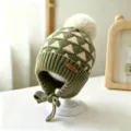 Close-up view of an olive green knit hat with cream triangle pattern, pom-pom and tied ear flaps - Baby 1-3 Years Elastic / Pineapple Grass Green