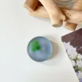 Close-up van een groen klavertje in een rond, mat blauwgrijs en doorschijnend decoratief object - Glitter Zwart