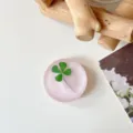 Bovenaanzicht van een rond, matroze harsdecor met een ingelegd groen klavertjevier - Wolk Flits Lichtroze