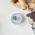 Close-up van een rond mat accessoire met een groene klaver, naast een boek met bloemenprint - Glitter Lichtpaars