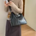Lifestyle view of a black faux-leather shoulder bag with flap detail, metal hardware and bear charm - With Pendant / Black