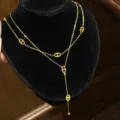 Close-up of a gold-tone double-layer chain with oval openwork charms and a small bead drop - Layered Pig Nose Tassel Style / Gold