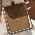Gold chain with a round blue gemstone pendant displayed in a dark brown velvet jewelry box - Six-Claw Blue Zirconia Necklace / Blue