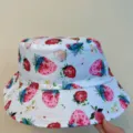 White bucket hat with all-over watercolor strawberry print, shown in hand against a beige backdrop - M (56-58cm) / White Strawberry Printed Style (20)
