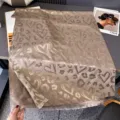 Dettaglio in piano di un tessuto tortora con cuori e macchie leopardate intrecciati, con frange - 185x65cm / Cammello