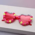 Pink transparent sunglasses with bead, star and festive letter decorations on a pale surface - Rose Red