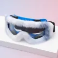 Close-up of blue ski goggles with fluffy white trim, dark lenses and a black elastic head strap - Blue Frame White Plush Pad