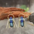 Détail des perles en verre bleu, des pendentifs rayés noirs et des tiges métalliques dorées sur bois - Style à Rayures Pendant / Bleu