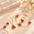 Jewelry set arranged on pale stone, showing red enamel four-leaf clovers on gold-tone pieces - Set / Red Clover