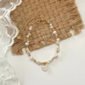 Vista dall’alto di un bracciale dorato con perle bianche e ciondoli a cuore su tessuto intrecciato - Bracciale Perla d'Acqua Dolce Conchiglia Cuore