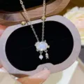 Close-up of a cat-shaped pendant with an oval white stone, dangling crystal and fishbone charm - Cat Eating Fish Pendant (X583) / Silver