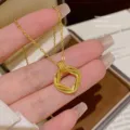 Close-up of a gold-tone necklace pendant with a textured square loop, held in a hand - X838 Style / Gold