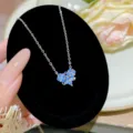 Close-up of a blue crystal flower pendant on a silver-tone chain against black velvet - Foldable Heart Four-Leaf Clover Style (X611) / Titanium Steel Silver