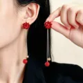 Orecchini a fiore rosso con catene argentate e pendenti rossi, indossati e tenuti vicino al viso - Stile Fiore in Nastro Rosso (F99)