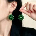 Primo piano di orecchini verdi lucidi a forma di nastro, indossati e tenuti accanto all’orecchio - Stile Fiore in Nastro a Stella Verde (0206)
