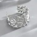 Primo piano di un bracciale rigido aperto argentato, con petali sagomati e dalla texture incisa - Argento