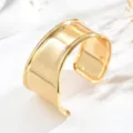 Bracciale rigido aperto dorato, con ampia superficie a specchio e bordi curvi su marmo bianco - Oro