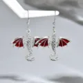 Primo piano di un paio di orecchini a drago argentati, con ali smaltate rosse, su supporto bianco - Stile Drago / Rosso