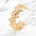 Primo piano di un bracciale aperto dorato con stelle marine unite e superficie martellata - Oro