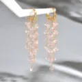 Orecchini dorati con fili di perline sfaccettate rosa chiaro, appesi a un supporto bianco - Rosa