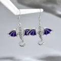 Coppia di orecchini a forma di drago argentati, con ali smaltate viola, appesi a un supporto bianco - Stile Drago / Viola