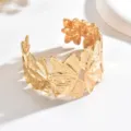 Bracciale rigido aperto dorato, largo e texturizzato, con foglie sovrapposte su fondo bianco - Oro