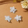 Tre fiori bianchi in pizzo e tulle con centri di perla sono disposti su una superficie color cuoio - Confezione da 1 Pezzo / Blu