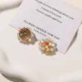 Close-up of two woven bead ornaments in cream, orange, pink and yellow on a white ceramic tray - Flower / 1 Piece