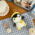 Overhead view of a plush penguin with a yellow hat, duck charm and hanging loop on checked fabric - Duck Penguin Style / Approx. 11cm / Yellow