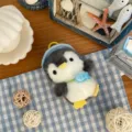 Overhead view of a gray and white plush penguin charm with a blue fish pendant and yellow clasp - Fish Penguin Style / Approx. 11cm / Blue