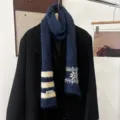 Écharpe en maille bleu marine, rayures ivoire et flocons, suspendue sur un manteau noir - Rayures de Flocons de Neige - Bleu Marine