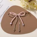 Close-up of a pink beaded bow with a pearl center, silver tubes, and dangling decorative ends - Pink