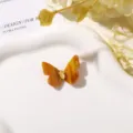Close-up van een amberkleurige harsvlinder met een gele druppelvormige steen op een wit schaaltje - 1 Stuk/Verpakking / Karamelbruin