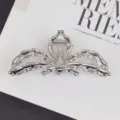 Dettaglio della clip argentata lucida con zampe scolpite, appoggiata su una pagina di rivista - Argento
