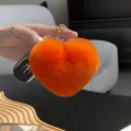 Primer plano de un corazón de peluche naranja y suave, con cadena dorada, sostenido en la mano - Naranja