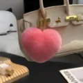 Primer plano de un suave colgante rosa en forma de corazón, con cadena dorada, en un bolso beige - Rosa