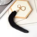 Primo piano della coda in finta pelliccia nera, con dettaglio di strass e moschettone dorato - Nero
