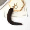Coda in ecopelliccia marrone scuro, chiusura dorata e dettaglio con strass, distesa su fondo bianco. - Caffè