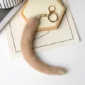Ciondolo di pelliccia beige, terminale con strass e moschettone dorato su un vassoio chiaro - Beige