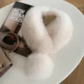 Flat lay of a fluffy ivory fur collar with a rounded pom-pom and soft beige shading - Almond